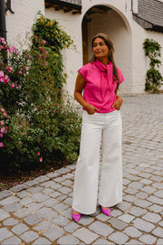 Pull à manches courtes noué porté par une femme, silhouette entière, pantalon blanc, ruelle