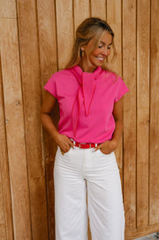 Pull à manches courtes noué porté par une femme, silhouette entière, pantalon blanc, mains dans les poches