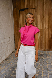 Pull à manches courtes noué porté par une femme, silhouette entière, pantalon blanc, porte en bois