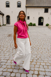 Pull à manches courtes noué porté par une femme, en marchant, pantalon blanc, pavés