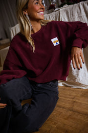 Pull effet polaire col rond bordeaux porté par une femme, vue de trois-quarts, jean foncé, sourire