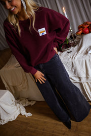 Pull effet polaire col rond bordeaux porté par une femme, vue de trois-quarts, table dressée, pantalon foncé