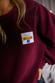 Pull effet polaire col rond bordeaux porté par une femme, vue rapprochée, étiquette colorée, maille bordeaux