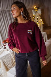 Pull effet polaire col rond bordeaux porté par une femme, vue de face, jean bleu, guirlande