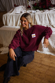 Pull effet polaire col rond bordeaux porté par une femme, assise, table dressée, jean foncé