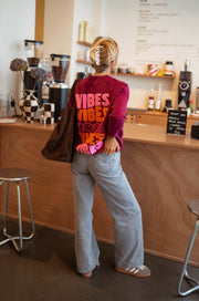 Pull à logo au dos bordeaux porté par une femme, vue de dos, logo VIBES, sac