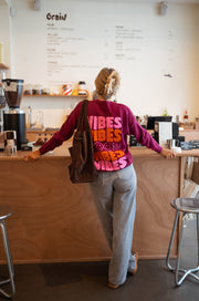 Pull à logo au dos bordeaux porté par une femme, vue de dos, sac, tabouret