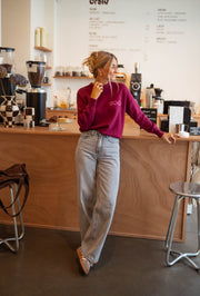 Pull à logo au dos bordeaux porté par une femme, vue de profil, comptoir, jean