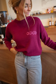 Pull à logo au dos bordeaux porté par une femme, vue de face, comptoir, jean clair