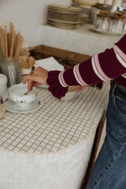 Pull moulant rayé à volants bordeaux et blanc porté par une femme, vue rapprochée à une table