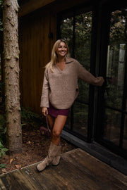Pull doux col V loose beige porté par une femme, vue de face, véranda, jupe bordeaux