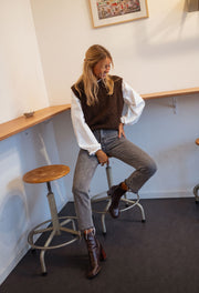 Pull sans manches effet mouton chocolat porté par une femme, assise, tabouret, bottines