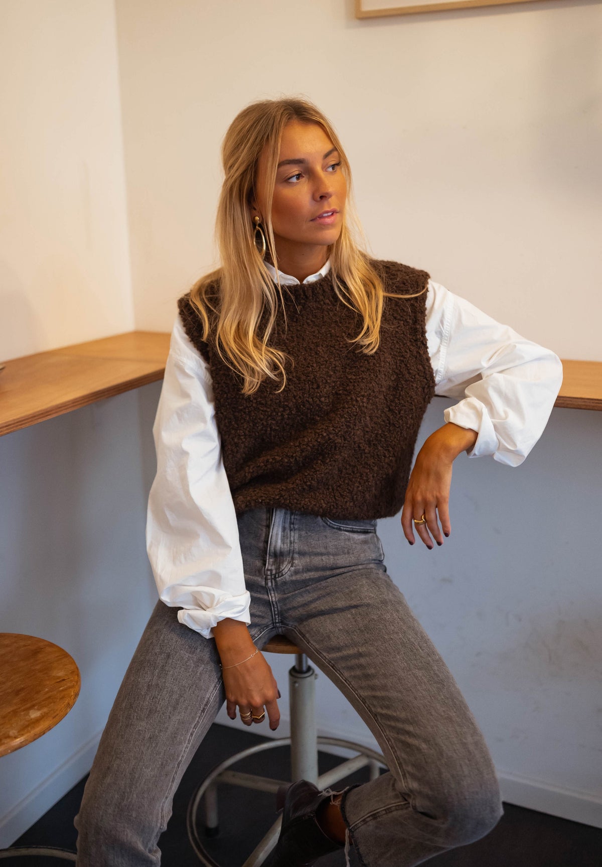 Pull sans manches effet mouton chocolat porté par une femme, assise, tabouret, chemise blanche
