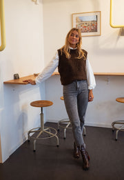 Pull sans manches effet mouton chocolat porté par une femme, silhouette entière, tabouret haut, jean
