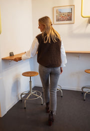 Pull sans manches effet mouton chocolat porté par une femme, vue de dos, tabouret, jean