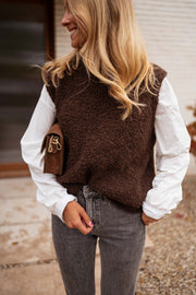 Pull sans manches effet mouton chocolat porté par une femme, vue de face, jean, mur blanc