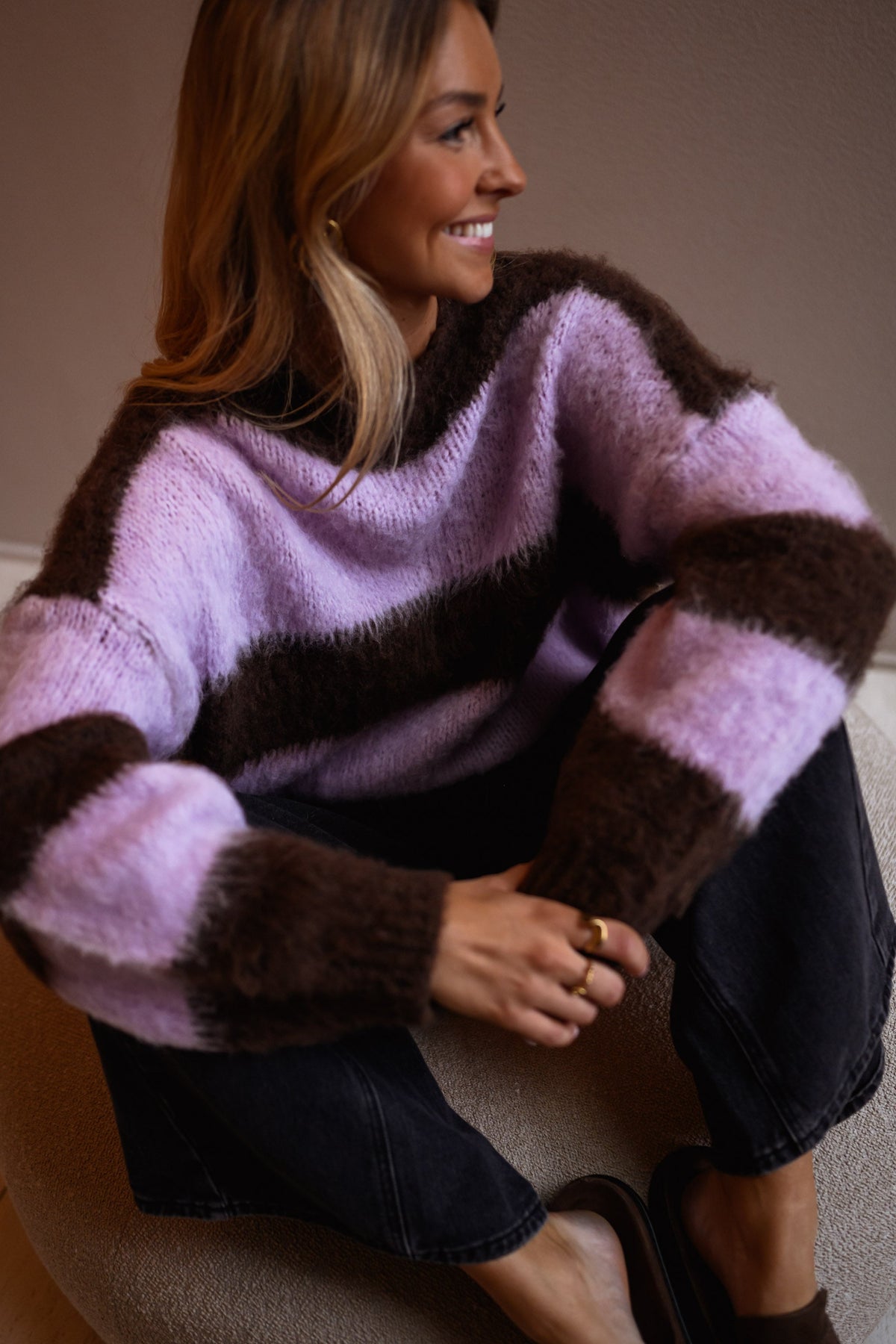 Pull légèrement ample col rond porté par une femme, vue rapprochée, rayures marron, pouf