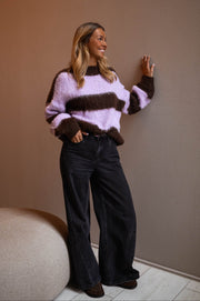 Pull légèrement ample col rond porté par une femme, vue de trois-quarts, mur taupe, pantalon noir