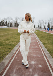 Pull court à cordons écru porté par une femme, vue de face, piste rouge, herbe