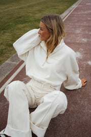 Pull court à cordons écru porté par une femme, assise, piste rouge, pantalon écru