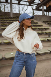 Pull court à cordons écru porté par une femme, vue rapprochée, casquette bleue, cheveux longs