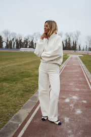 Pull court à cordons écru porté par une femme, vue de face, piste rouge, pantalon écru