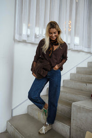 Pull doux à manches longues marron porté par une femme, vue de trois-quarts, escalier, sac marron