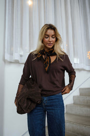 Pull doux à manches longues marron porté par une femme, vue de face, foulard au col, escalier