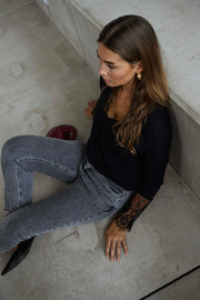Pull col V à dentelle noir porté par une femme, assise, escalier, jean gris