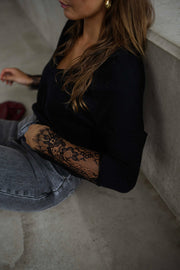 Pull col V à dentelle noir porté par une femme, vue rapprochée, manches en dentelle, cheveux longs