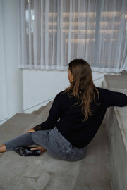 Pull col V à dentelle noir porté par une femme, vue de dos, escalier, rideaux blancs