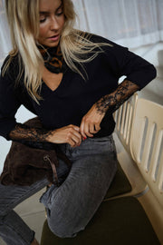 Pull col V à dentelle noir porté par une femme, assise, banc kaki, manches en dentelle