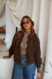 Pull doux à boutonnage mandarin marron foncé porté par une femme, assise, lunettes de soleil