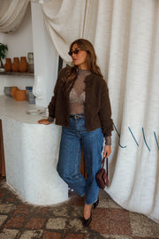 Pull doux à boutonnage mandarin marron foncé porté par une femme, silhouette entière, sac à la main