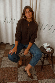Pull doux à boutonnage mandarin marron foncé porté par une femme, assise, sur un tabouret