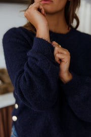 Pull doux à boutons latéraux bleu marine porté par une femme, vue rapprochée, main au menton