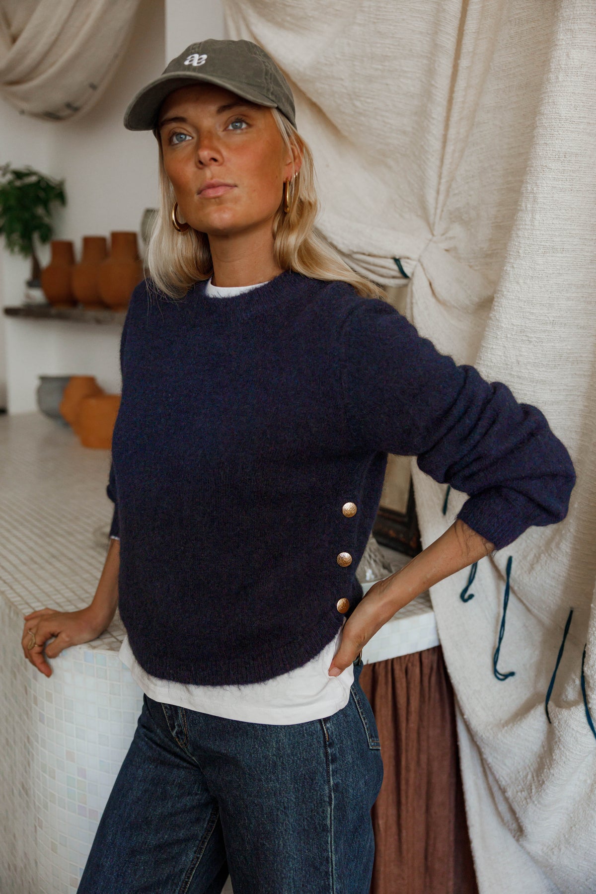 Pull doux à boutons latéraux bleu marine porté par une femme, vue de face, casquette