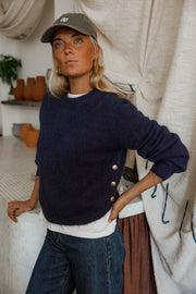Pull doux à boutons latéraux bleu marine porté par une femme, vue de face, casquette