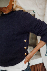 Pull doux à boutons latéraux bleu marine porté par une femme, gros plan du côté avec boutons dorés