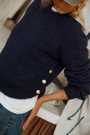 Pull doux à boutons latéraux bleu marine porté par une femme, détail des boutons dorés, bras sur la hanche