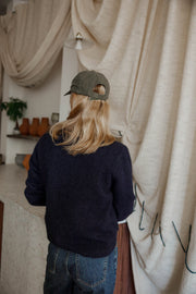 Pull doux à boutons latéraux bleu marine porté par une femme, vue de dos, casquette