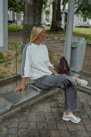 Pull à bandes manches trois-quarts porté par une femme, assise, sur un banc, jean gris, sac marron