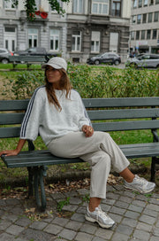 Pull à bandes manches trois-quarts porté par une femme, assise, sur un banc, pantalon clair, baskets