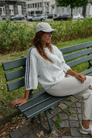 Pull à bandes manches trois-quarts porté par une femme, assise, assise de côté, casquette, banc vert