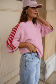 Pull à manches trois-quarts porté par une femme, vue de face, casquette rose, bras levé