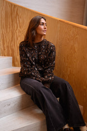 Pull léopard à col rond porté par une femme, assise, escalier clair, sourire