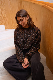 Pull léopard à col rond porté par une femme, assise, escalier en bois, pantalon noir