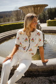 Pull fleuri à manches courtes porté par une femme, assise, fontaine, sourire
