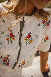 Pull fleuri à manches courtes porté par une femme, vue rapprochée, fleurs brodées, boutons