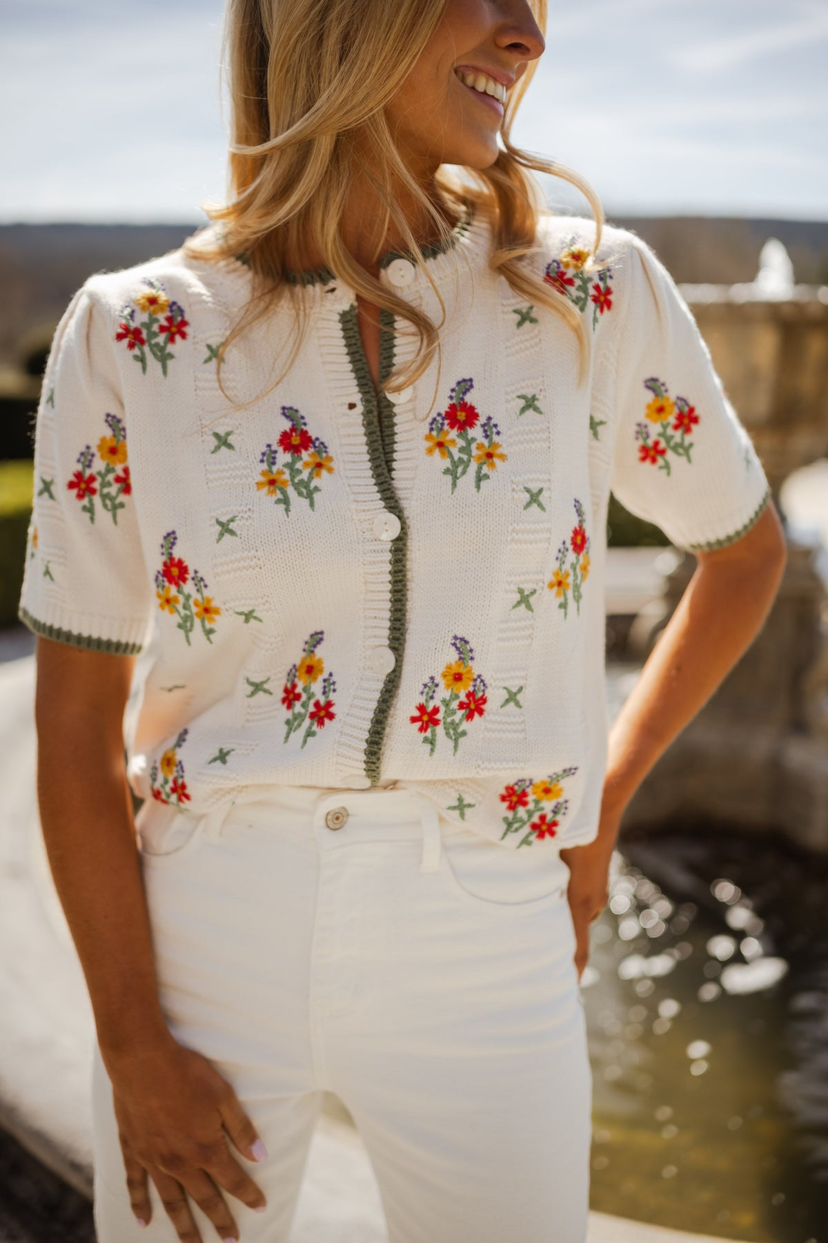 Pull fleuri à manches courtes porté par une femme, vue de face, fleurs brodées, pantalon blanc